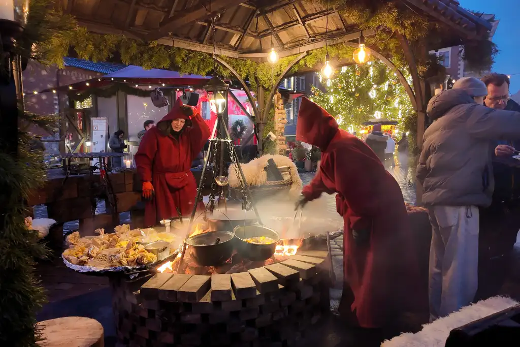 People in cloaks cook food at Riga Christmas Market